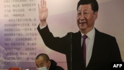 中国辽宁省沈阳市的一家书店里一名戴着口罩的读者坐在中国国家领导人习近平的大幅画像前。（2020年4月23日）