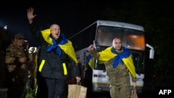 身披蓝黄色乌克兰国旗的战俘步下巴士,热烈期待与亲人团聚。(乌克兰总统新闻处提供)