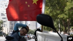 北京街头一名快递员在电动车旁休息。(2020年9月2日)