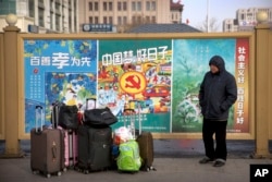 2018年2月9日,一名男子站在北京火车站外面的一堆行李旁边,准备回家过春节。旁边是种种宣传口号。