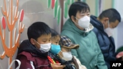 2025年1月6日,在中国东部浙江省杭州市一家医院的儿科,戴着口罩的儿童在成人的陪同下等待医护人员的诊治。(法新社)