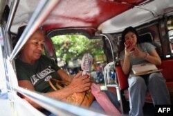 Seorang perempuan menggunakan kipas angin elektrik untuk mengusir hawa panas di dalam angkutan jeepney di tengah gelombang panas di Manila, Senin, 29 April 2024. (Foto: Ted Aljibe/AFP)