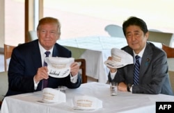 在东京附近的高尔夫球场俱乐部共进午餐时，唐纳德·川普和安倍晋三在白色球帽上签名，帽子上印着“唐纳德和晋三使同盟更伟大”（2017年11月5日）