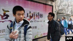 资料照片:北京一所学校外面,少年们走过宣传牌,牌上写着中英文口号“点亮中国梦 知识改变命运 付出收获财富”。(2018年3月12日)