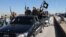 FILE - Islamic State militants pass by a convoy in Tel Abyad town, northeast Syria.