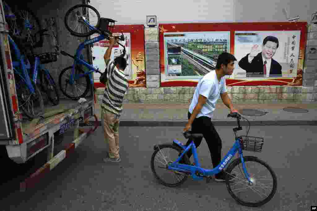 北京街头关于中国特色社会主义、四个自信和“中国梦 人们的梦”的宣传画前面,工人们从卡车上卸下共享单车公司的自行车(2018年8月22日)。