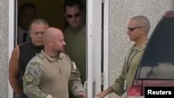 塞萨尔·萨尤克(穿黑衣者)被捕后被带离佛罗里达州密拉玛的联调局设施。(2018年10月26日)