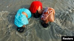 Các phụ nữ đạo Hindu đi hành hương nhúng đầu xuống nước sông Hằng