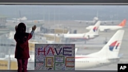 在马来西亚吉隆坡国际机场,一名女孩透过窗户眺望停机坪,身旁是公众写的“保持希望”的标语牌。