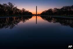 在华盛顿国家大草坪上,黎明之前,华盛顿纪念碑和绿树的影子投射在映影池(2016年4月17日)。