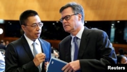 资料照片:美国驻WTO大使谢伊(右)在瑞士日内瓦举行的世界贸易组织(WTO)会议上与中国驻WTO大使张向晨交谈。(2018年7月26日)