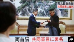 Hình ảnh chiếu trên màn hình tivi ở Tokyo, Nhật Bản cho thấy lãnh tụ Triều Tiên Kim Jong Un (phải) và Tổng thống Hàn Quốc Moon Jae-in trao đổi các văn kiện được kí ở Bình Nhưỡng, Triều Tiên, ngày 19 tháng 9, 2018.