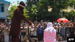 Seorang petugas sedang melaksanakan hukuman cambuk pada seorang pemudi Aceh yang bersalah melanggar Syariat Islam karena berkencan sebelum menikah. Hukuman dilaksanakan disebuah panggung terbuka di luar sebuah masjid di Banda Aceh,1 Agustus 2016.