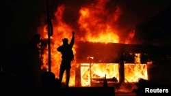 Một người biểu tình vung tay trước những tòa nhà đang bốc cháy trong các cuộc biểu tình liên quan đến cái chết của George Floyd ở Minneapolis, bang Minnesota, ngày 30 tháng 5, 2020.