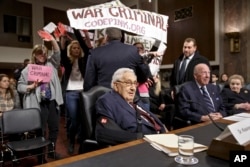 基辛格(左)和舒尔茨与奥尔布赖特三位前国务卿在参议院军事委员会作证时,抗议者干扰会场。(2015年1月29日)