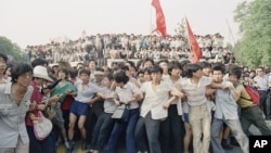 资料照片:1989年6月3日在北京人民大会堂附近,支持民主的抗议者手挽手阻止愤怒的人群追逐撤退的士兵。(美联社)