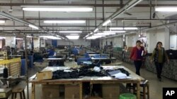 中国广东省中山市南朗镇翠亨制包厂工人罢工,几名工人走过车间里处于停工状态的工作台,2015年3月26日(资料图)