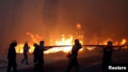 Firefighters, soldiers and local residents carry a hose as a wildfire burns in the town of Rafina, near Athens, Greece, July 23, 2018.