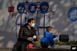 2021年11月17日, 在北京前门街道的一幅抗疫宣传画下,一名幼儿在一名女子的看顾下玩耍。(美联社)