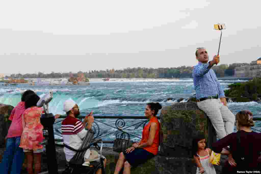 国际游客在加拿大安大略省的尼亚加拉瀑布市的马蹄瀑布旁边摆姿势照相。