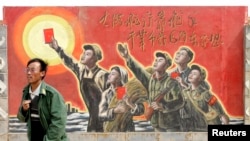 资料照:一名男子走过宁夏银川街头郊区的一处描写中国文革的宣传画。(2007年4月25日)