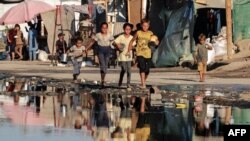 资料照片:在加沙地带中部代尔巴拉赫,巴勒斯坦儿童携带容器走过污浊的废水,前往一个食品分发点。(2024年7月19日)