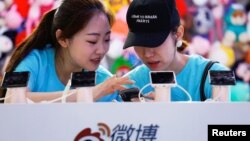 2018年4月27日,在北京举行的全国移动互联网大会(GMIC)期间,工作人员在新浪微博的摊位上使用智能手机。一个人的帽子上有英文,意思是“我是来让人心碎的”。