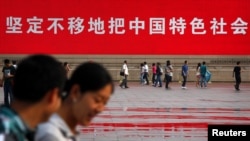 资料照：人们走过北京天安门广场竖立的一幅宣传中国特色社会主义道路的巨幅标语。（2012年6月3日）