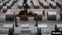 资料照:中国重庆钢铁厂一名工人走过钢卷存放地。(2018年8月6日)