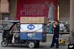 2018年6月27日,北京的一幅毛泽东像和毛泽东诗词牌匾下面,快递员正准备送货。