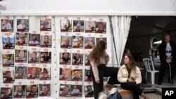 以色列特拉维夫两名女子坐在被哈马斯拘押在加沙的人质照片的海报旁。(2025年1月17日)