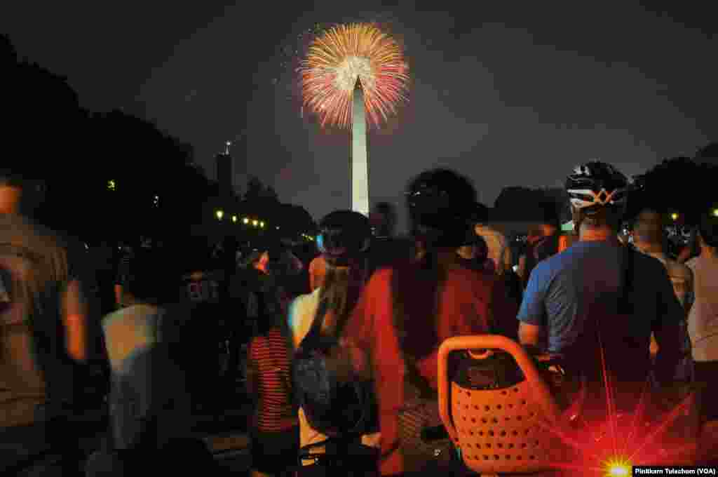 美国人在首都华盛顿的国家大草坪上观赏焰火,礼花在华盛顿纪念碑上空绽放(2017年7月4日)。