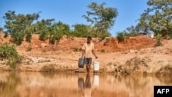 Seorang pria mengambil air di sebuah kolam untuk ternak-ternaknya di Matobo, Matabeleland, 10 Mei 2024. (Foto: Zinyange Auntony/AFP)