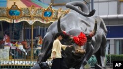 2018年7月9日,一名妇女在北京一家零售和批发服装商场外面铜牛雕塑旁边。