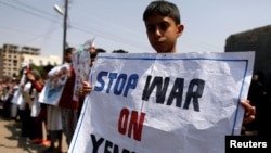 也门首都萨那,一名男孩在联合国办公室外举着标语牌,谴责空袭行动。(2018年8月13日)