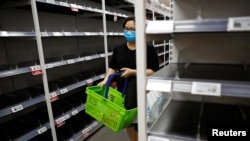 一名戴口罩的新加坡妇女星期六(2月8日)在商店购物。货架上的方便面和罐头食品似乎已被抢购一空。