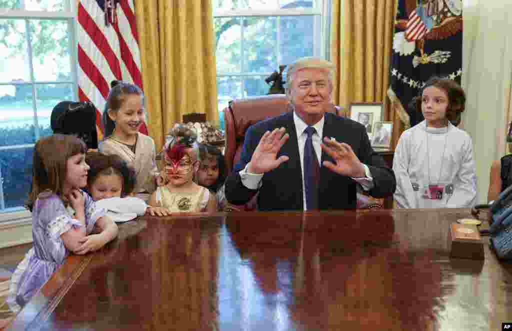 2017年10月27日,川普总统在白宫椭圆形办公室对媒体人员的孩子们谈话时抬手示意。这些孩子应邀到白宫过万圣节,穿着节日的服装。