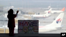 在吉隆坡国际机场,一个女孩站在签名板旁,签名板上写着“抱有希望”