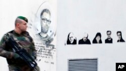 Một binh sĩ Pháp tuần tiễu bên cạnh một bức tranh vẽ chân dung các họa sĩ biếm họa bị giết, Charb (trái), Honore, Wolinski, Cabu, Charb và Tignous bên ngoài tòa soạn cũ của Charlie Hebdo, 1 năm sau cuộc tấn công ở Paris, ảnh chụp ngày 7/1/2016. (AP Photo/Francois Mori)