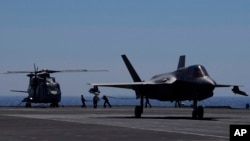 资料照 - 英国航母伊丽莎白女王号上的机械师正给一架停留在甲板上的直升机加油,旁边一架F-35隐身战机准备起飞。