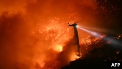 2025年1月11日,加利福尼亚州曼德维尔峡谷社区和恩西诺附近的火势正在蔓延,一架消防直升机正在喷水。