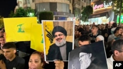 约旦河西岸城市拉马拉举行支持真主党的集会,巴勒斯坦抗议者举着真主党旗帜和印有在以色列空袭中丧命的真主党领导人纳斯鲁拉照片的海报。(美联社:2024年9月28日)