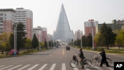 人们戴着口罩推车从朝鲜首都平壤柳京饭店前的一条路上走过。(2020年4月28日)