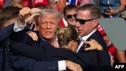 도널드 트럼프 미국 공화당 후보가 7월 13일 펜실베이니아에서 열린 선거 행사에서 비밀 경호원들에게 둘러싸인 채 얼굴에 피를 흘리며 무대에서 내려오고 있다.