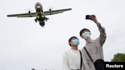 两名戴着口罩的青年正在以即将降落在台湾台北松山机场的飞机做背景自拍。(2020年3月29日)