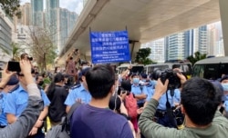 大批在场戒备的警员多次向西九法院大楼外排队的市民高举蓝旗及紫旗，警告聚集的市民涉嫌非法集结，高呼的口号涉嫌违反国安法 (美国之音/汤惠芸)