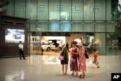 2018年7月5日,一些女士在北京一家高档购物中心的特斯拉展厅外观看智能手机。