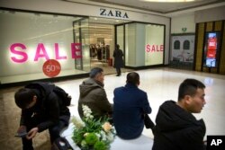 2018年1月12日,在北京一家购物中心的Zara商店外,购物者们看着他们的智能手机。