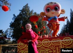 在春节前夕,在北京地坛庙会,一位妇女在猴子造型前面摆姿势照相(2016年2月5日)