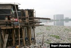 Anak-anak berdiri di dalam rumahnya di atas danau yang tercemar sampah di kawasan kumuh, Jakarta Utara. (Foto: REUTERS/Supri)